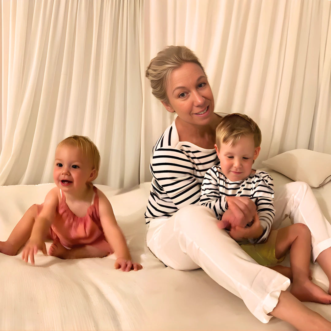 Female Fashion entrepreneur Sue Carter, founder of CARI luxury design maternity & new mother & baby brand, sitting on white sofa for a mother & babies photoshoot