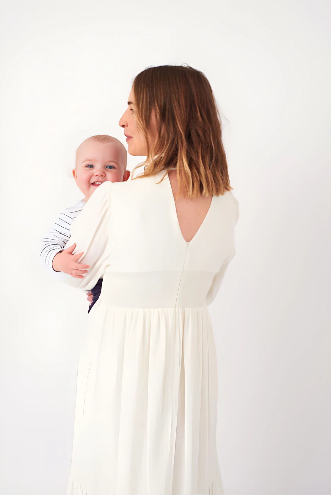 Beautiful stylish Notting HIll mother with baby in ivory white maxi dress for new baby photoshoot that is designed for pregnancy and breastfeeding friendly with discreet private zips - luxury style brand for motherhood fashion 
