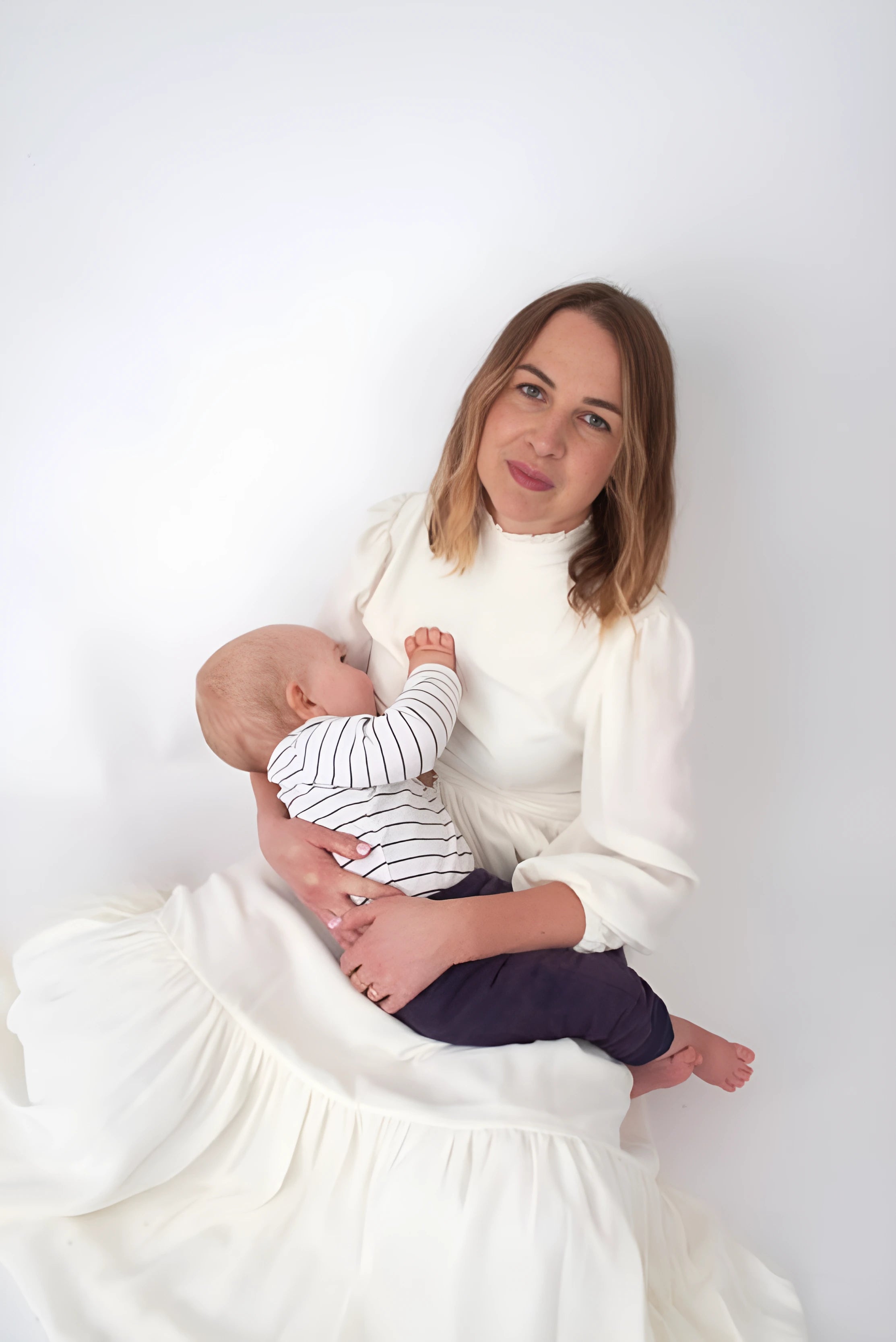 Stylish breastfeeding new mother with baby in ivory white maternity and nursing dress with hidden zips making it easy to feed her baby discreetly at an event - luxury designer maternity clothes mother & baby brands in UK Ireland a perfect dress for a maternity photoshoot and newborn shoot elegant style